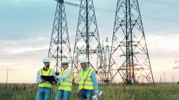 Trois ingénieurs marchent près des lignes électriques sur le terrain. Industrie électrique, concept de production d'énergie électrique. — Video