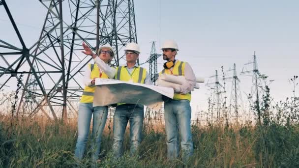 Les gens travaillent sur le terrain près de la ligne électrique, vérifiant le plan. Industrie électrique, concept de production d'énergie électrique. — Video