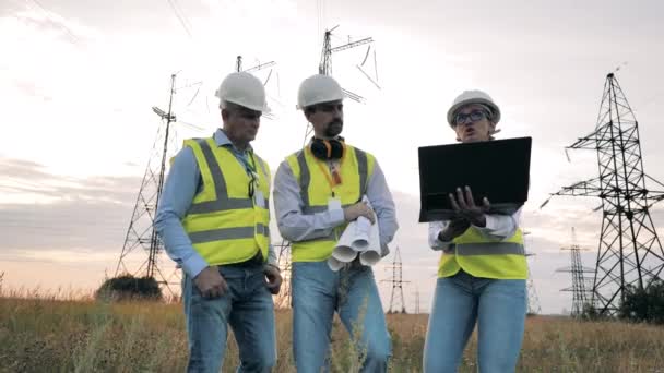 Trabalhadores da energia caminham em um campo, trabalhando com laptop. — Vídeo de Stock