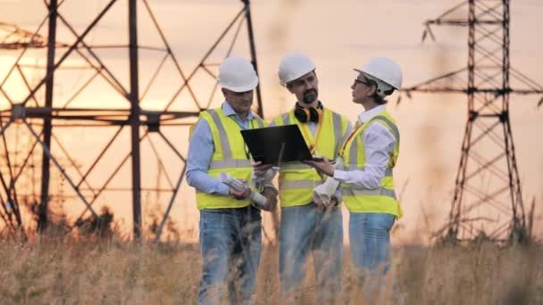 Arbetare i uniform pratar medan de håller sig nära kraftledningar. Elindustri, koncept för elenergiproduktion. — Stockvideo