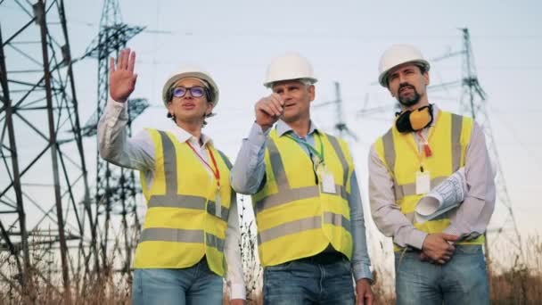Elindustri, koncept för elenergiproduktion. Elektriska arbetare står i ett fält medan du tittar på kraftledningar. — Stockvideo