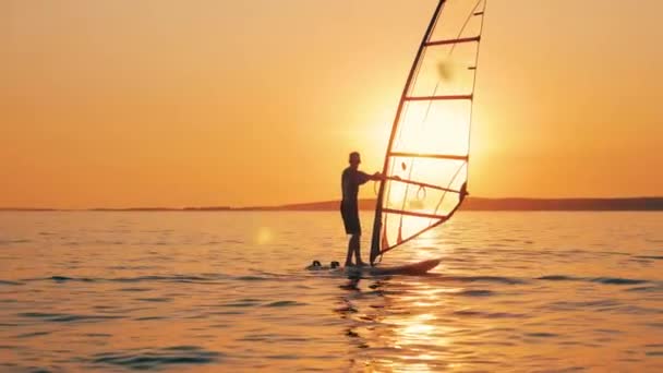Два чоловіки пливуть на дошках віндсерфінгу під час заходу сонця — стокове відео