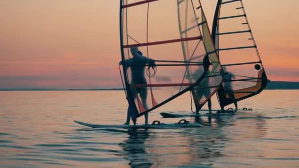 Виндсерфингисты плывут по озеру на закате — стоковое видео