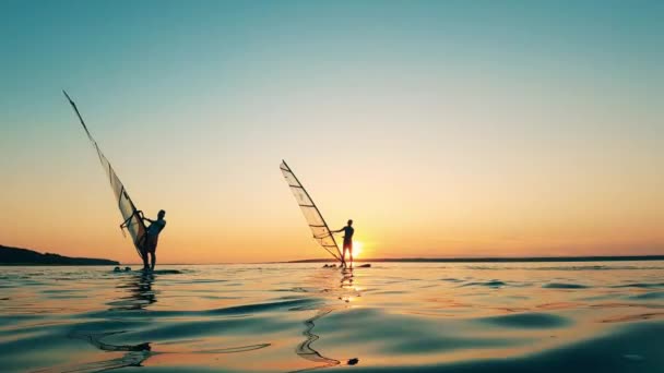 Två män vindsurfar i en sjö vid solnedgången. — Stockvideo
