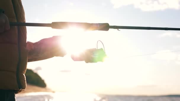 Bobina de pesca se tambalea en manos masculinas al atardecer — Vídeo de stock