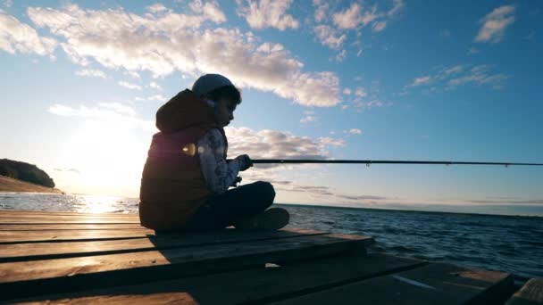 Un ragazzo sta pescando sulla banchina alla luce del sole — Video Stock