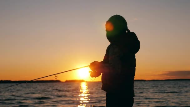 Egy kölyök horgászbotot vezet naplementekor. — Stock videók