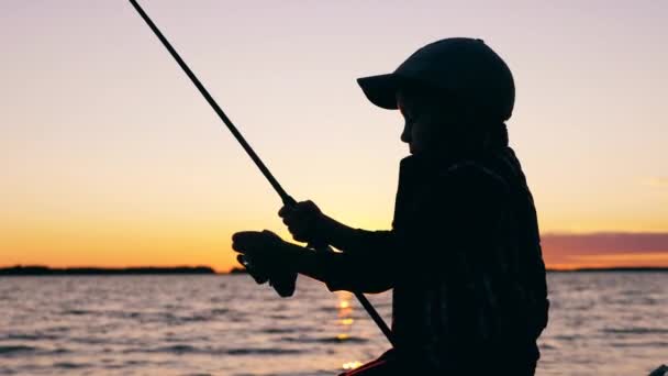 Un niño está usando una caña de pescar para pescar al atardecer — Vídeo de stock