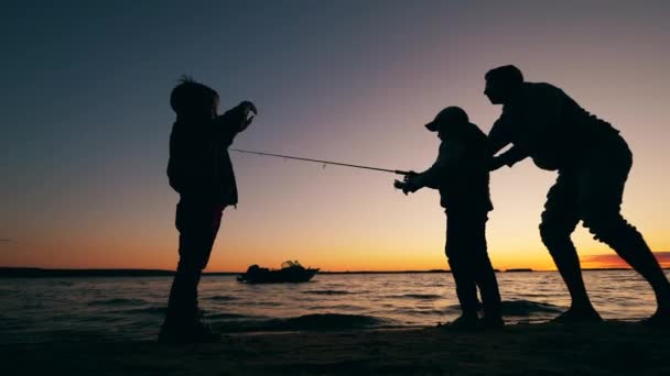 Copiii și tatăl lor sunt fericiți în timp ce pescuiesc la apus — Videoclip de stoc