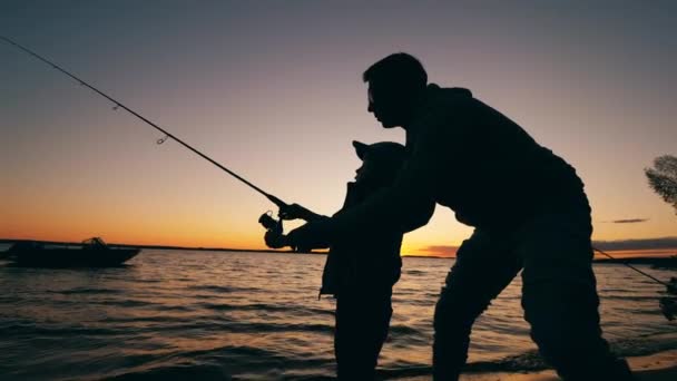 Ένας άντρας βοηθάει το γιο του με το ψάρεμα το ηλιοβασίλεμα. — Αρχείο Βίντεο