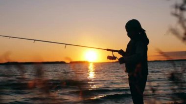 Gün batımı gölü ve elinde olta tutan bir çocuk.