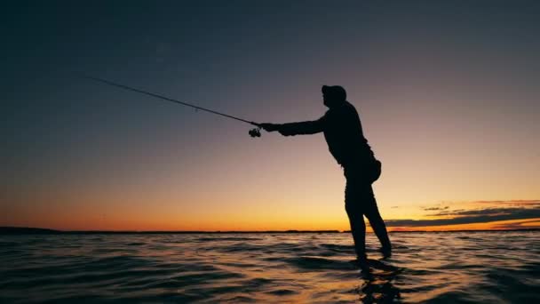 日落时，一个男人正在把一根钓竿抛入水中 — 图库视频影像