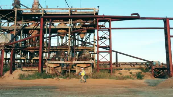 Two specialists are passing by a massive construction in the sand — Stock Video