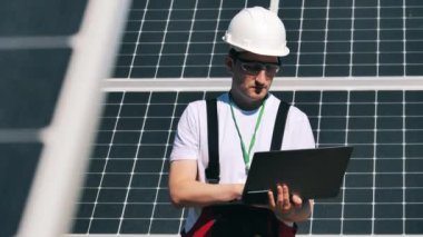 Dizüstü bilgisayarı olan teknisyen güneş panellerini inceliyor. Güneş enerjisi santrali yakınında alternatif enerji işçisi.