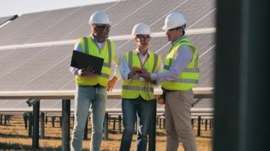 Yenilenebilir enerji, güneş santrali, yeşil elektrik konsepti. Bir grup mühendis güneş panellerinin yanında durup konuşuyorlar.