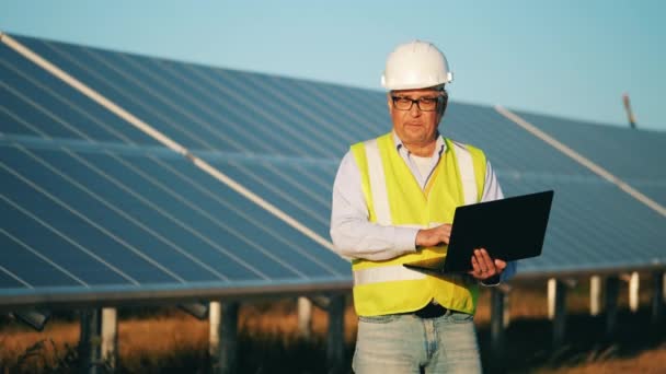 Solar engineer voert data in op de laptop terwijl hij buiten is. Alternatief energiewerker in de buurt van zonne-energiecentrale. — Stockvideo