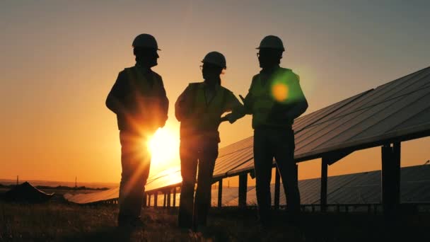 Podsvícení inženýři diskutují při západu slunce vedle solárních panelů. Obnovitelná energie, solární elektrárna, koncept zelené elektřiny. — Stock video