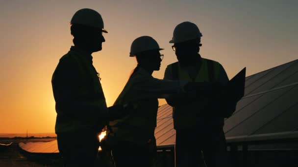 Puesta de sol con equipo de ingenieros discutiendo cerca de paneles solares — Vídeos de Stock