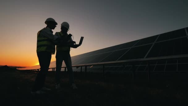 Dos ingenieros de energía están discutiendo junto a las baterías solares — Vídeo de stock