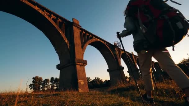 A lady with hiking inventory is walking under an old bridge — Stock Video