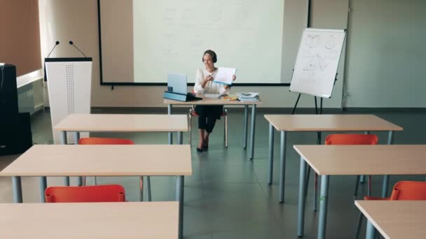 Aula vuota con un'insegnante donna che conduce una classe online in essa — Video Stock