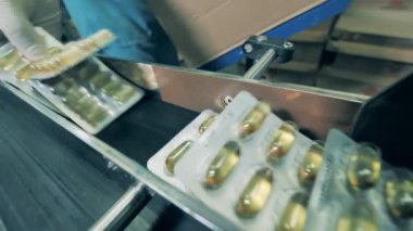 İşçi taşıyıcıdan kapsüllü kabarcıklar topluyor. İlaç fabrikası üretim hattı.