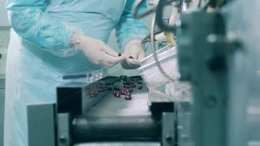 Sağlık çalışanı konveyördeki kapsülleri kontrol ediyor. Bir ilaç tesisinde ilaç üretim hattı..