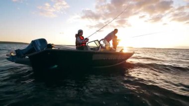 İki çocuk babalarıyla yelkenlide balık tutuyor.