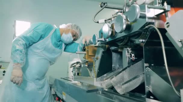 Un pharmacien travaille avec une machine tandis que les capsules se déplacent sur une ligne. Ligne de production d'usine pharmaceutique. — Video