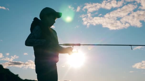 En pojke rullar upp en fiskespö i solljus — Stockvideo