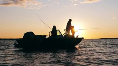 Çocuklar gün batımında babalarıyla teknede balık tutuyorlar.