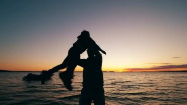 Bir adam çocuğunu gölün yanında döndürüyor.