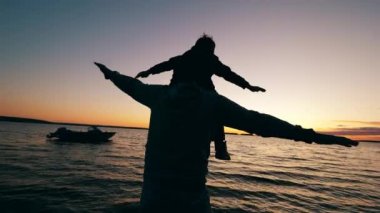 Omuzlarında bir çocukla oturan baba gün batımını izliyor.