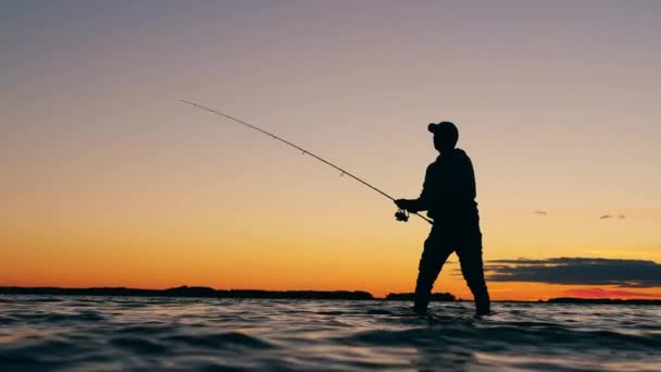 Rybář si při stání ve vodě vytahuje rybářský prut. — Stock video