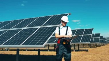 Erkek işçi bir güneş enerjisi çiftliğini gözlemliyor. Modern güneş panelleri, ekolojik dost enerji üretimi.