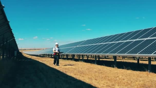 Hombre trabajador está caminando a lo largo de una central solar — Vídeo de stock