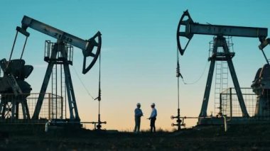 Teknisyenler iki petrol pompa ünitesi arasında konuşuyorlar. Petrol kuyusu, ham petrol, sondaj kulesi, petrol sahası, ham petrol fiyatı, petrol ve doğalgaz, petrol varili, petrol endüstrisi konsepti.