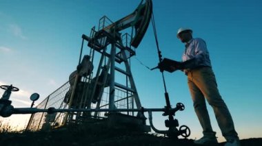 Erkek mühendis, çalışan bir petrol pompalama ünitesini gözlemliyor.