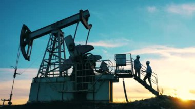 Erkek teknisyenler bir petrol pompalama ünitesini kontrol ediyorlar.