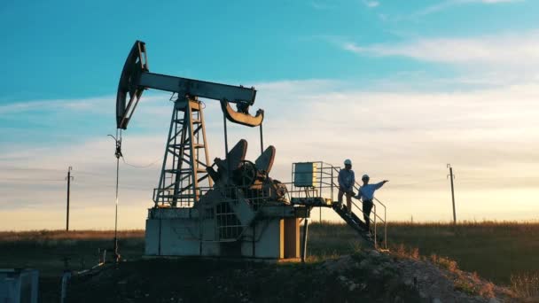 Unidade de bombeamento de óleo com dois engenheiros discutindo planos sobre ele — Vídeo de Stock