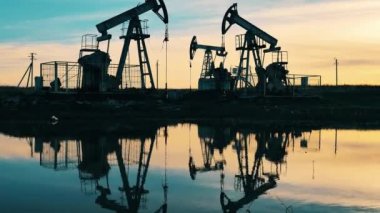 Gün batımında birden fazla metal yapılar petrol pompalıyor. Petrol kuyusu, ham petrol, sondaj kulesi, petrol sahası, ham petrol fiyatı, petrol ve doğalgaz, petrol varili, petrol endüstrisi konsepti.
