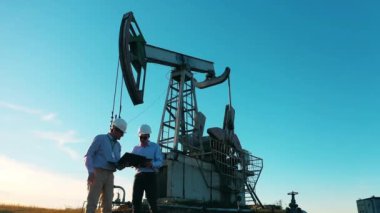 Petrol kuyusu, ham petrol, sondaj kulesi, petrol sahası, ham petrol fiyatı, petrol ve gaz, petrol varili, petrol endüstrisi konsepti. İki mühendis bir petrol pompalama ünitesinin yanında konuşuyorlar.