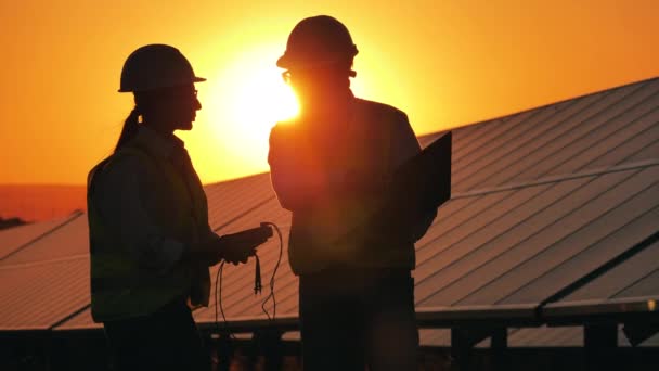 Dos trabajadores de la energía están hablando junto a las baterías solares iluminadas por el sol — Vídeos de Stock