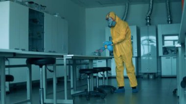 Tehlikeli madde giysisi giyen işçiler laboratuarın yüzeyini temizliyor.