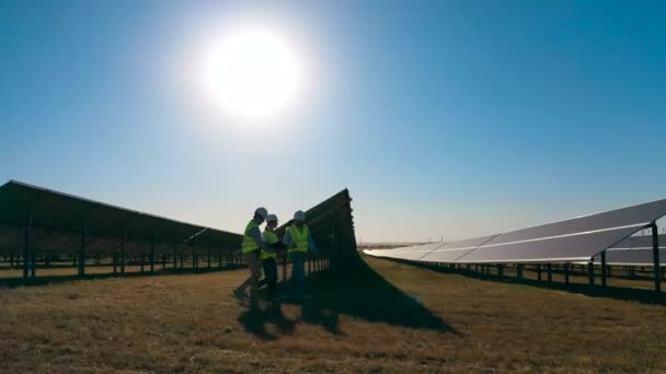 Energetik-Spezialisten gehen an einem Solarkraftwerk auf einem Solarfeld entlang. — Stockvideo