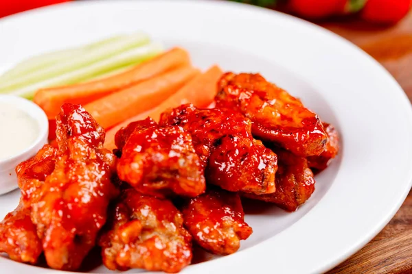 Buffalo chicken wings with blue cheese dip, carrots and celery sticks on white plate. Close up