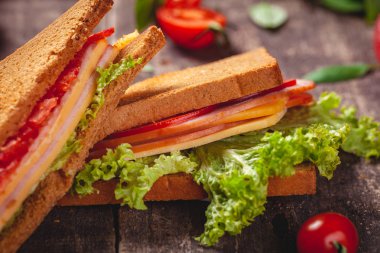 Jambon, peynir, domates ve marul ile sandviç ahşap rustik masada bırakır. Yakın çekim