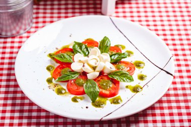 Geleneksel İtalyan caprese salatası dilimlenmiş domates, mozzarella peyniri, fesleğen ve beyaz tabakta pesto sosu. Kapat.