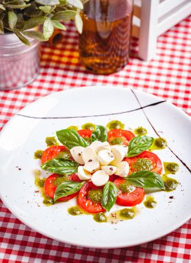 Geleneksel İtalyan caprese salatası dilimlenmiş domates, mozzarella peyniri, fesleğen ve beyaz tabakta pesto sosu. Kapat.
