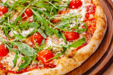 Domatesli İtalyan pizzası, mozarella peyniri ve ahşap kesim tahtasında roka. Kapat.